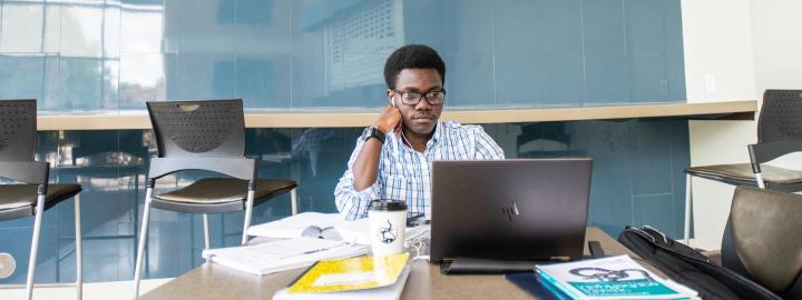 Graduate student studying with a laptop and books.